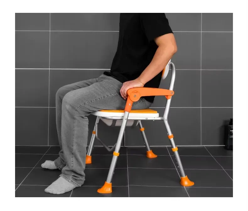 Existing AryMD orange folding bath chair image showing adult seated on orange folding bath chair in tile setting